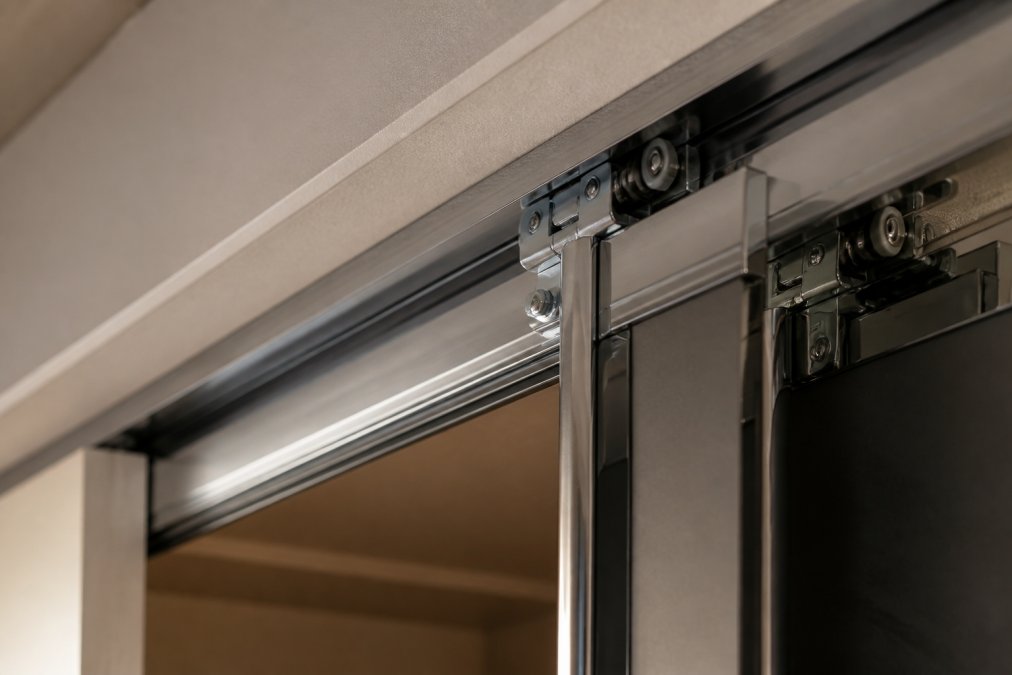 Close-up of fitted wardrobe sliding door track system with smooth metal runners and hinges in polished finish, showing internal mechanism detail with soft studio lighting