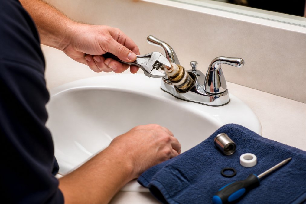 Maintenance technician using an adjustable wrench to remove a bathroom faucet cartridge onto a clean towel