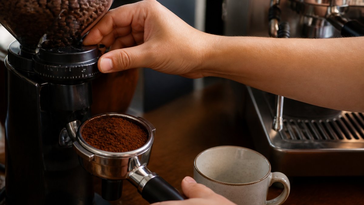 Hands adjusting a coffee grinder dial with fresh grounds in a portafilter ready for brewing
