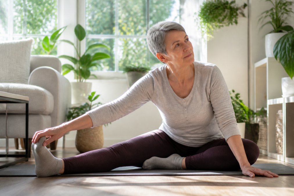 Mature adult performing gentle stretching or low-impact movement in a bright home environment with natural sunlight streaming through windows