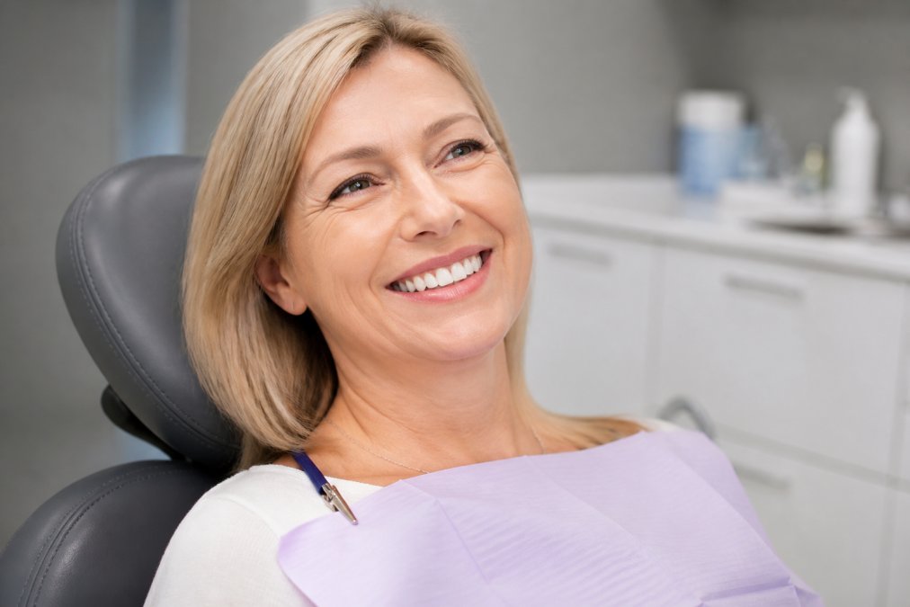 Patient displaying natural-looking smile with dental crowns and restorations seamlessly blended with remaining natural teeth in modern clinical setting with soft natural lighting