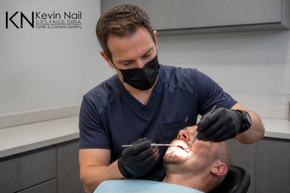 Patient in dental chair during post-operative follow-up examination, dentist carefully inspecting healing implant site with professional lighting and sterile instruments