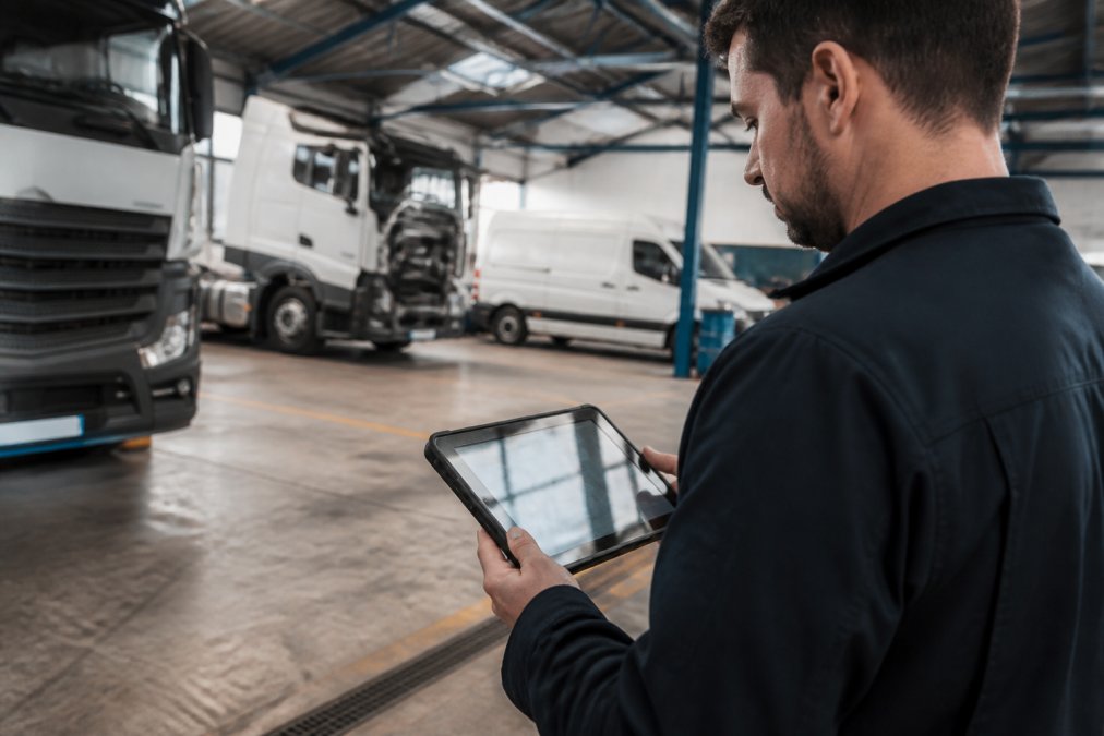 Fleet manager reviewing maintenance dashboard on tablet in aircraft hangar with parked planes visible in background, natural hangar lighting