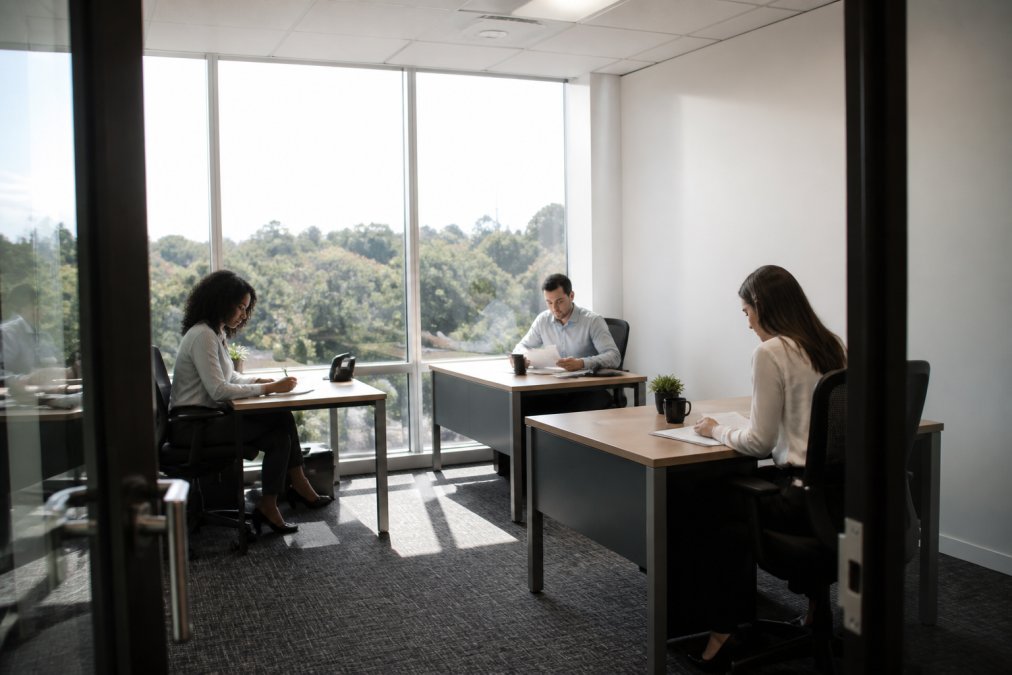 Three professionals collaborating in a bright private office featuring flexible office solutions and modern desks.