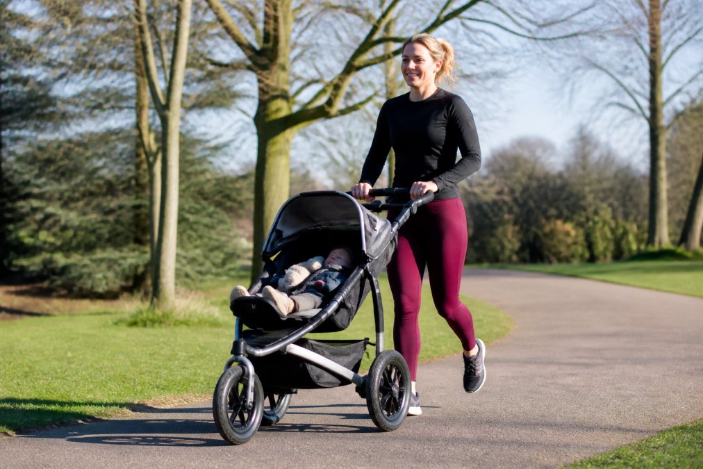 Parent jogging with a running pram on a park path on a sunny day, showing proper posture and pram positioning