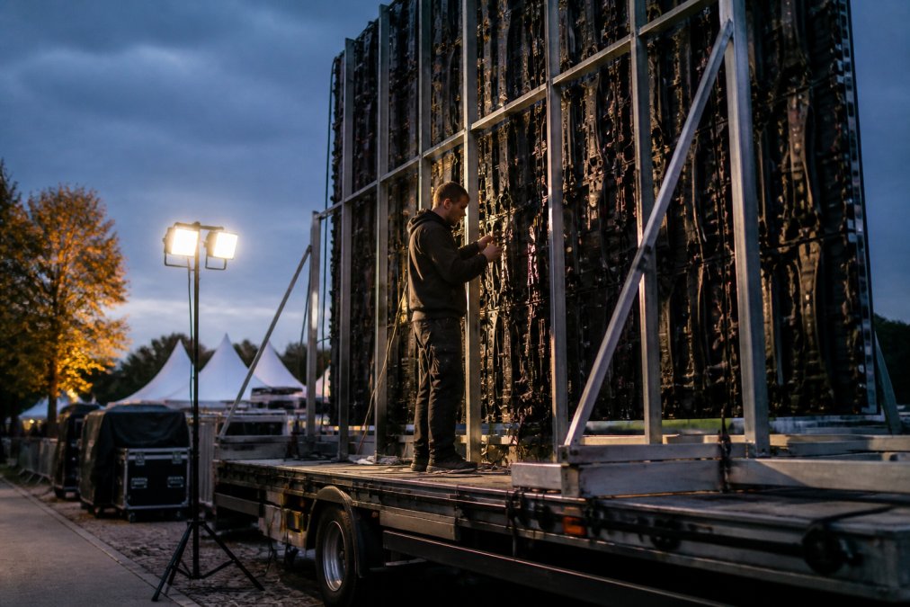 Professionele technicus die een groot outdoor LED-scherm op een aanhangwagen installeert bij een openlucht evenement, met zichtbare controlekabels en werklampen die de installatie verlichten