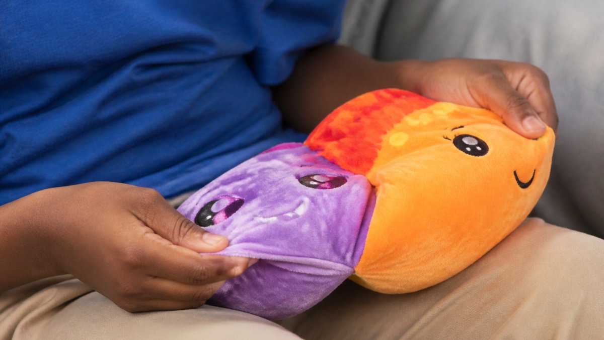 Child's hands flipping a reversible plush toy inside out, showing the transformation from one character design to another, with soft fabric and bright colours visible