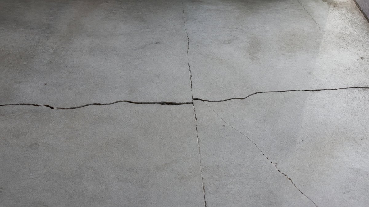 Close-up of concrete floor slab showing multiple crack patterns including horizontal, vertical, and diagonal cracks with visible width variations and texture detail