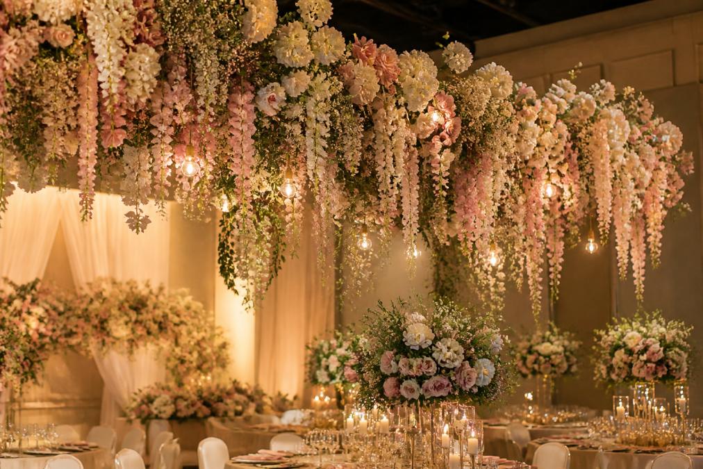 Elegant cascading floral installation with soft pink and white blooms creating a statement backdrop, suspended at varying heights with warm ambient lighting highlighting the delicate textures and depth of the arrangement