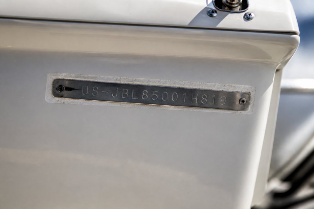 Close-up of a boat's hull identification number (HIN) plate on the starboard side with clear alphanumeric characters etched into the fiberglass, bright natural sunlight highlighting the details