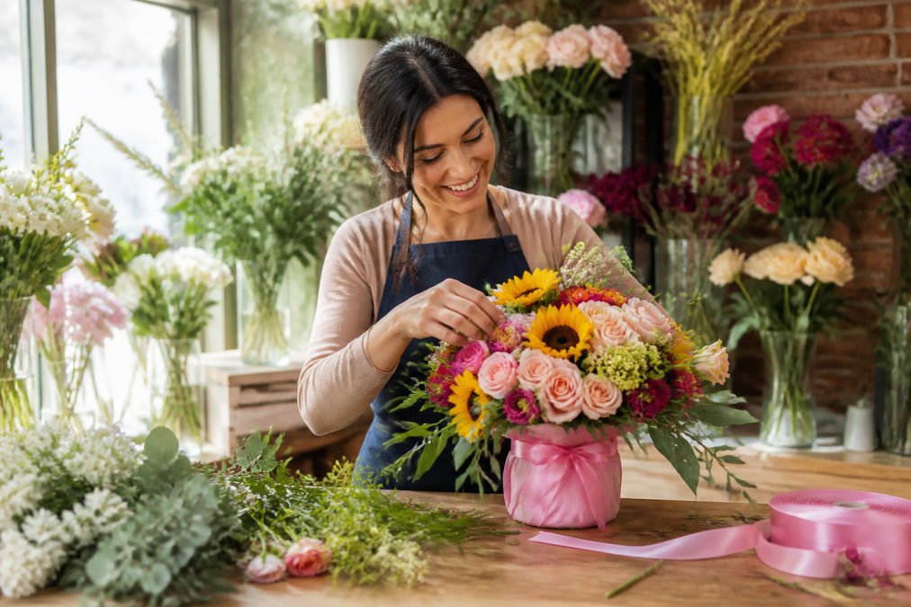 A friendly florist arranges a bright birthday bouquet for local flower delivery services in a sunny shop.