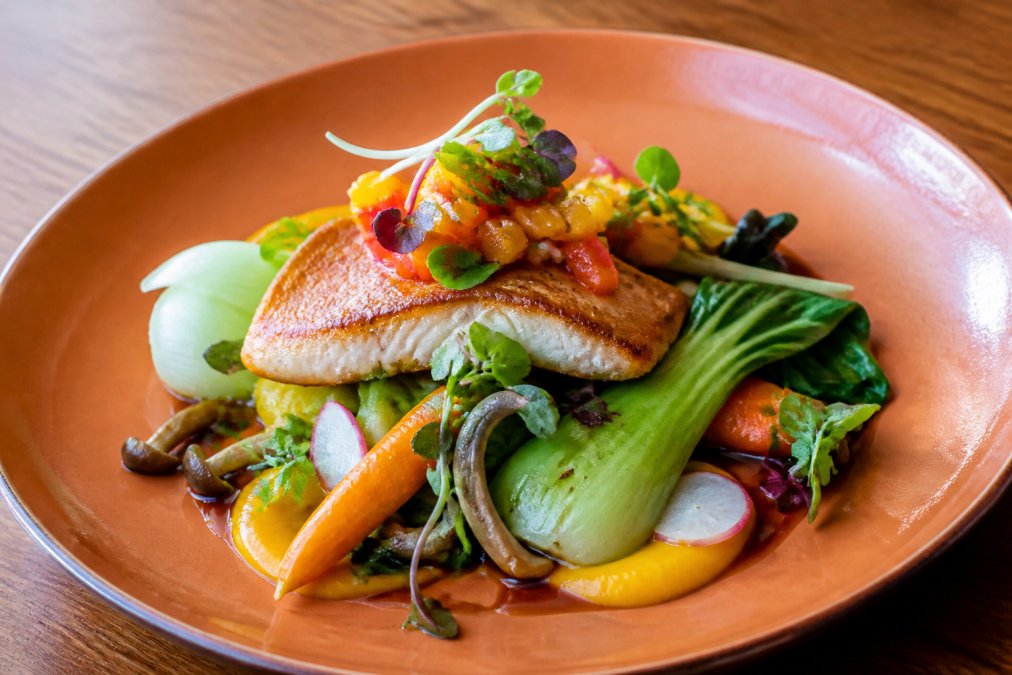 Vibrant plated Asian fusion dish with fresh seafood, colorful garnishes, and artistic presentation on a warm-toned plate with soft natural lighting highlighting ingredient quality
