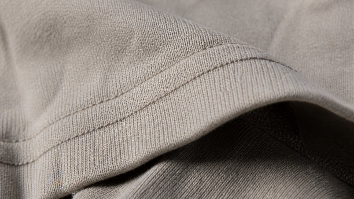 Close-up of heavyweight cotton fabric texture showing visible weave structure, thread density, and reinforced double-needle stitching detail under natural light