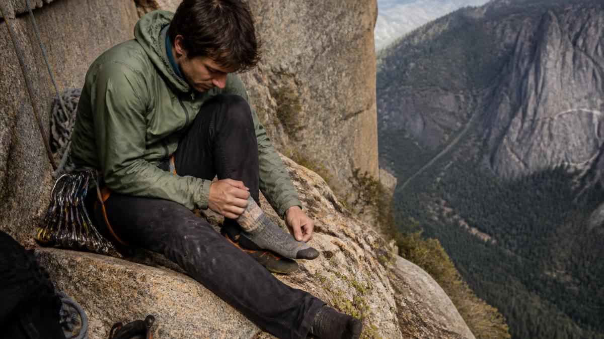 Climber sitting on a granite ledge checking their foot for blisters during a multi-pitch climb
