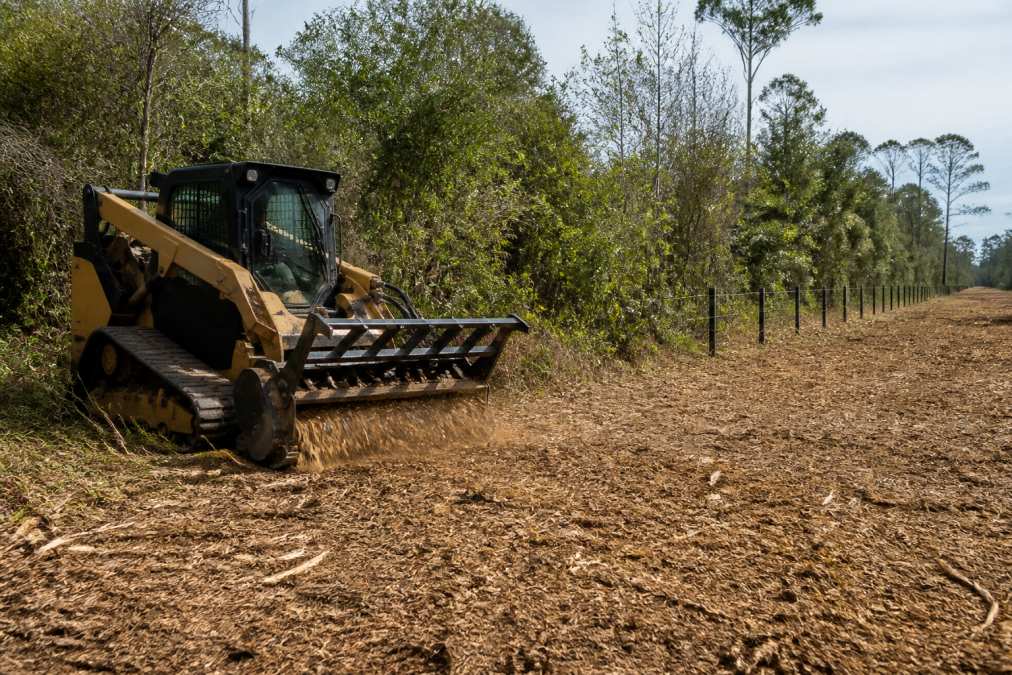Tracked skid steer performing forestry mulching on thick brush and trees in a rural East Texas landscape