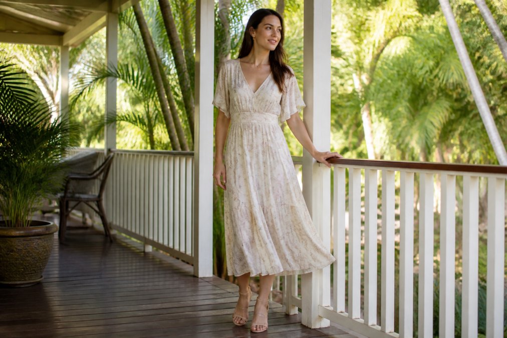 Woman wearing a flowing light-colored formal wear midi dress on a shaded tropical veranda