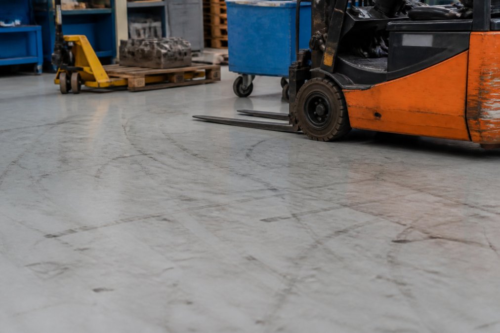 Fortelock vs Danish Floor System: Sammenligning 3 Værksted med tunge maskiner, gaffeltrucks og palletrucks på et robust PVC-gulv, der viser daglig industriel belastning med mærker fra hjul og værktøj