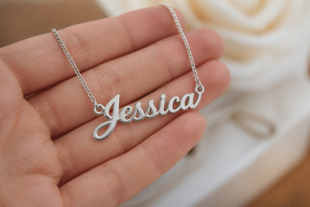 Close-up of a custom name necklace pendant being held in natural light, showing fine detail of polished stainless steel and crisp cursive lettering, with soft focus background