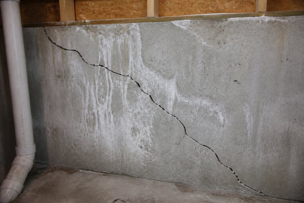 Close-up of a visible diagonal crack running across a poured concrete basement wall in a residential home, with slight efflorescence staining around the crack