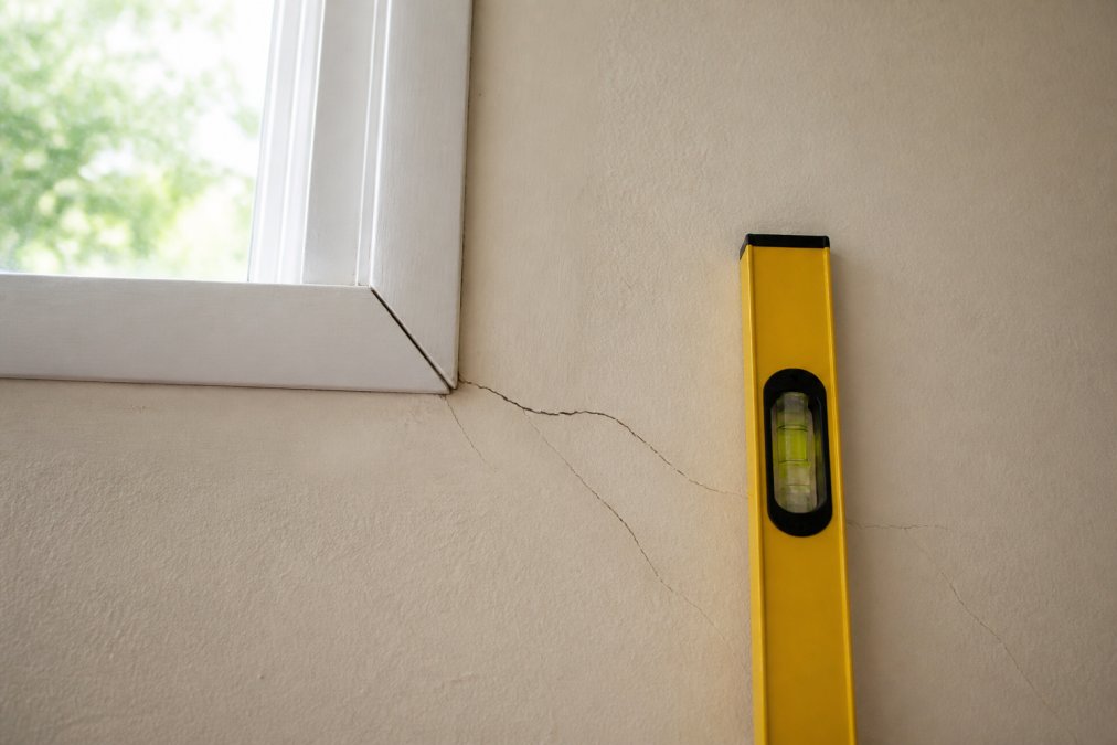 Diagram showing diagonal wall cracks and a level tool indicating foundation settling symptoms