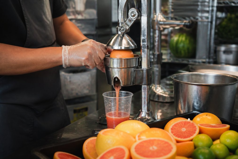 Close-up of fresh citrus fruits being cut and pressed into juice, showing vibrant colors and pulp mid-extraction in a professional juice bar setting