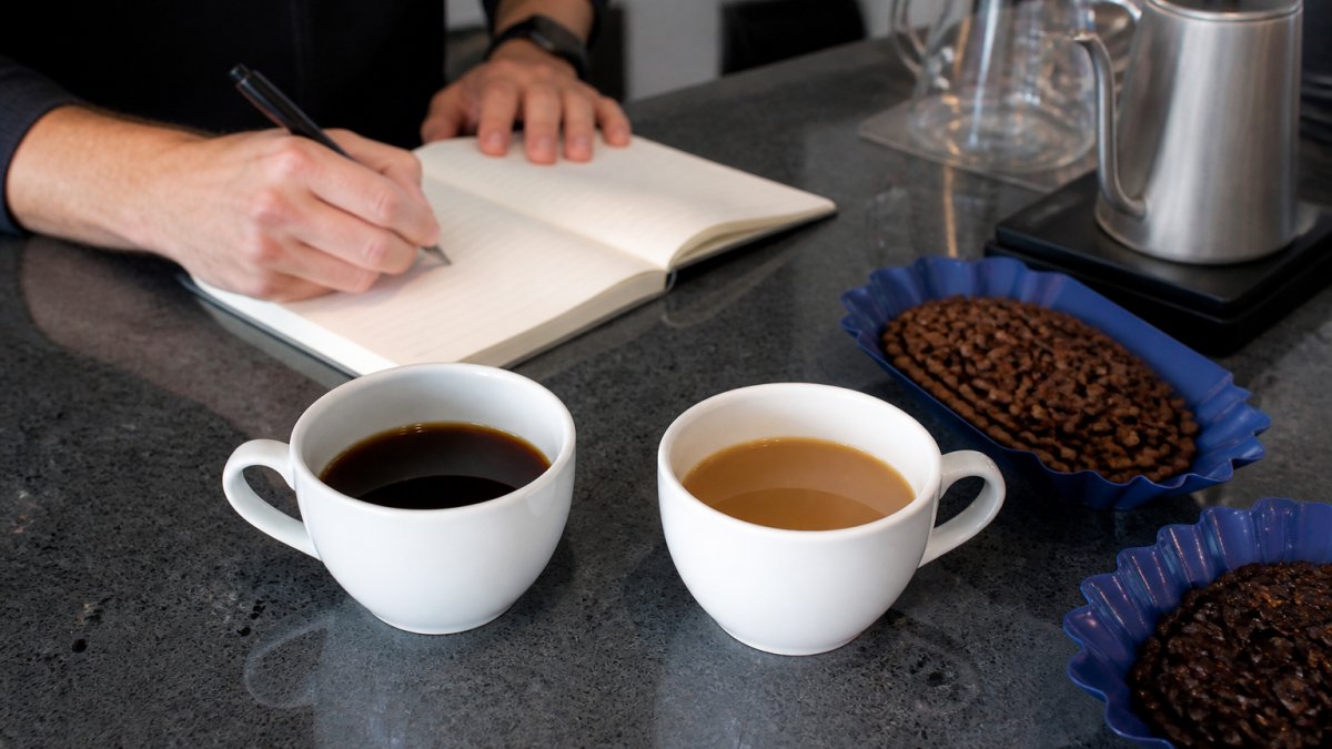 Two white coffee cups with different roasts and a notebook for recording tasting notes on a kitchen counter.