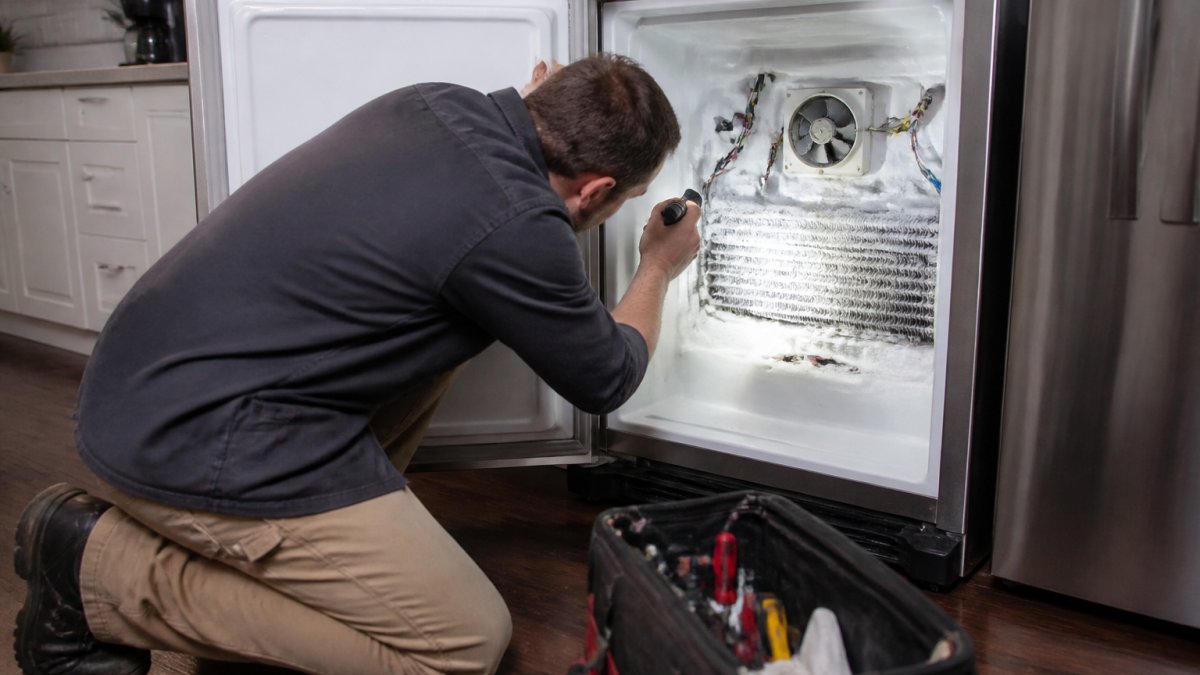 Homeowner using a flashlight to inspect a frozen evaporator fan when a fridge not cooling properly