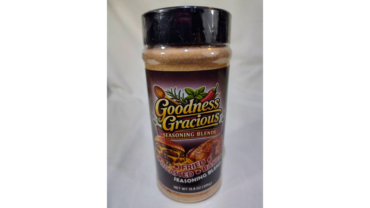 Home cook seasoning grilled chicken and fresh vegetables with vibrant gourmet spice blend in a bright, modern kitchen, herbs and spices visibly falling onto golden-brown food