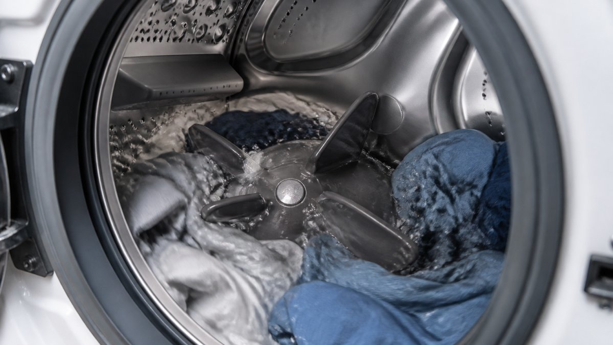 Close-up of front-load washer drum interior showing impeller design with ribbed fins and wet clothes tumbling in horizontal rotation