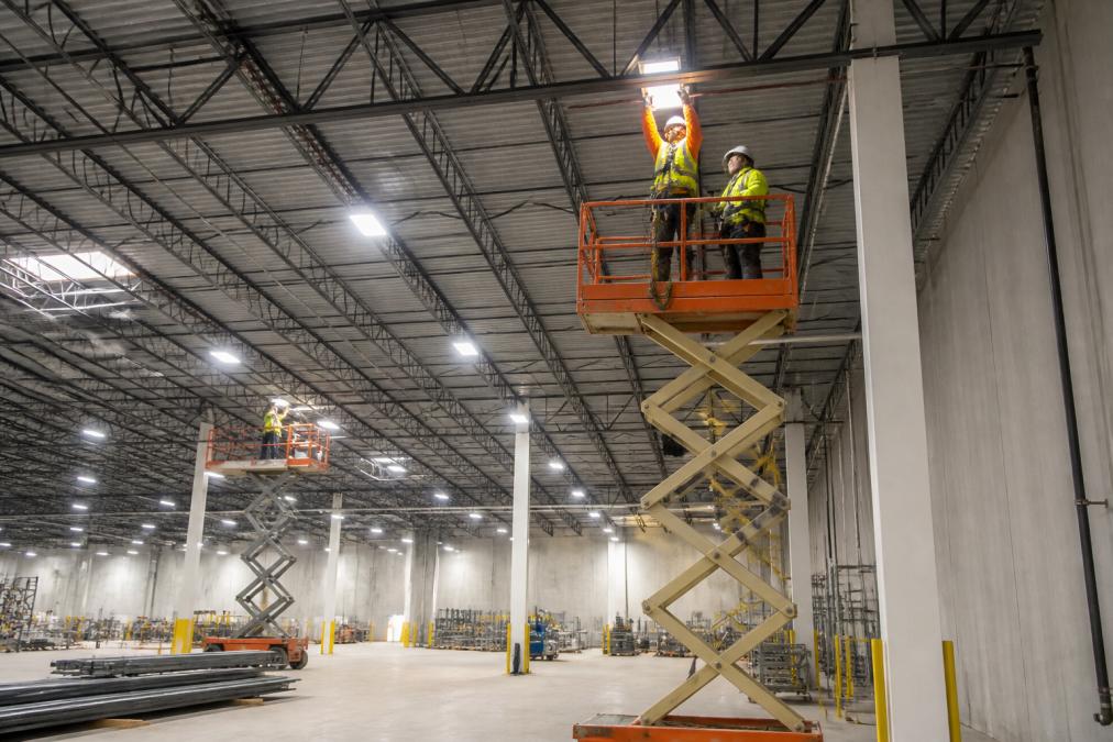 Technicians using lifts to install LED high-bay lighting as your energy efficiency partner in a large warehouse.