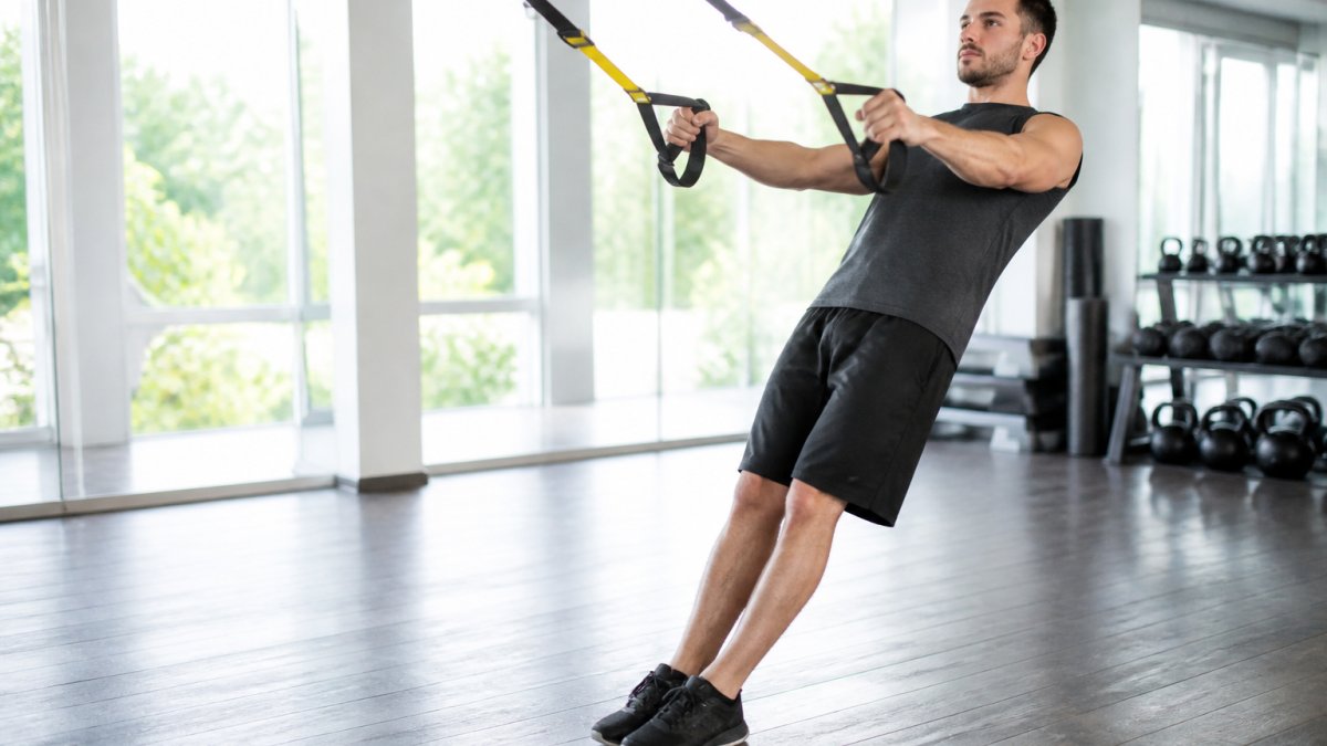 Person performing a controlled chest press with suspension straps in a bright fitness studio with proper body alignment