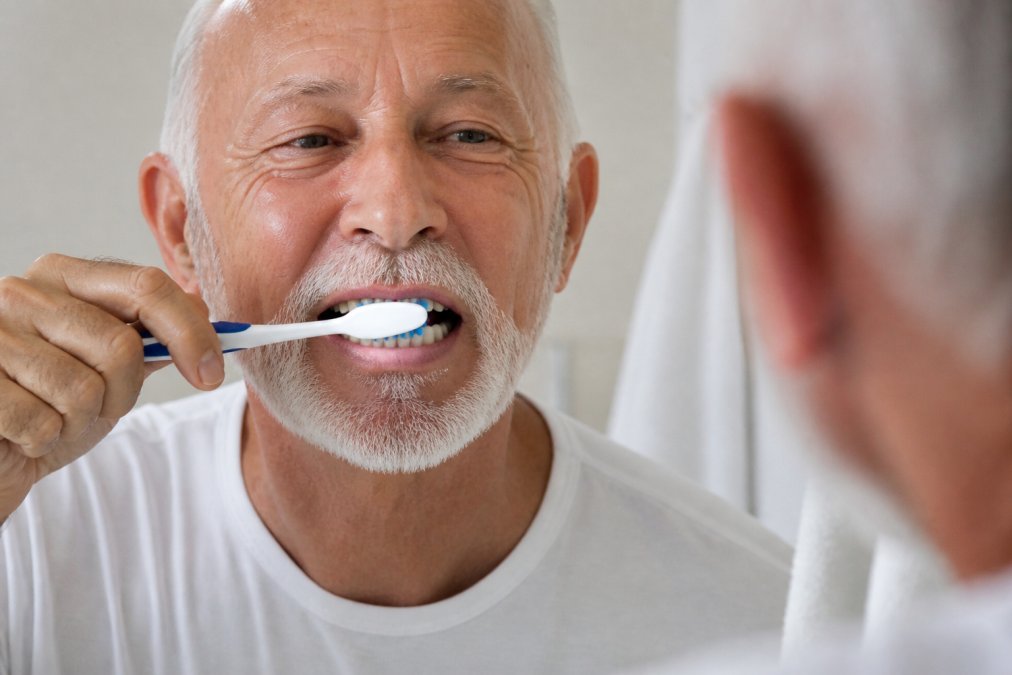 Close-up of senior's hands demonstrating proper brushing technique with soft toothbrush and flossing with dental floss on natural teeth and restorations