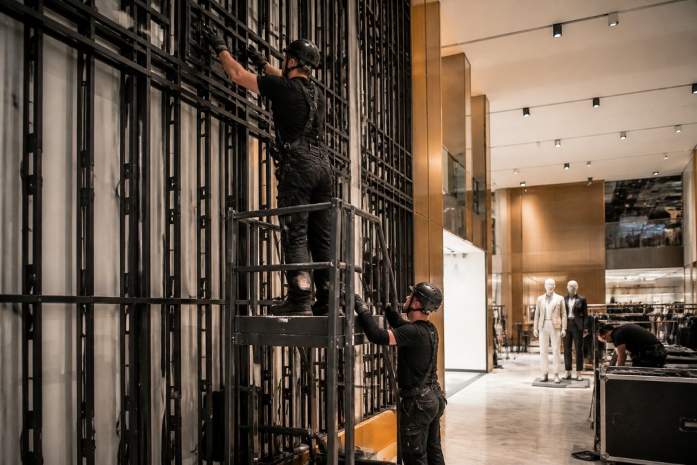 Professional technicians installing large LED screen in retail space, using mounting equipment and safety gear, demonstrating the setup process with precision and care
