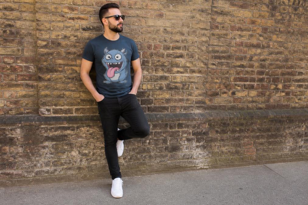 Person wearing a bold funny animal graphic t-shirt with a cartoon creature design, styled casually with dark jeans and white trainers, standing in natural daylight near a brick wall showing how the design catches attention and becomes the focal point of the outfit