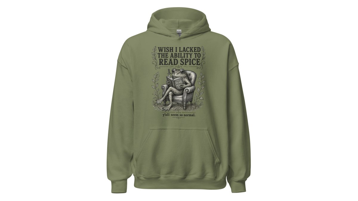 Person wearing a vintage-style graphic hoodie featuring a frog on a gothic throne, sitting in a cozy reading nook with a book and a mug of coffee, warm lamp lighting