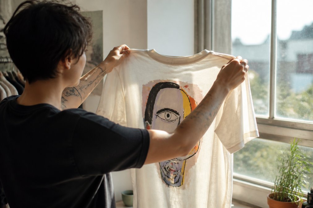 Person inspecting the fabric quality of a graphic t-shirt as a galartsy alternative in a bright, sunlit room.