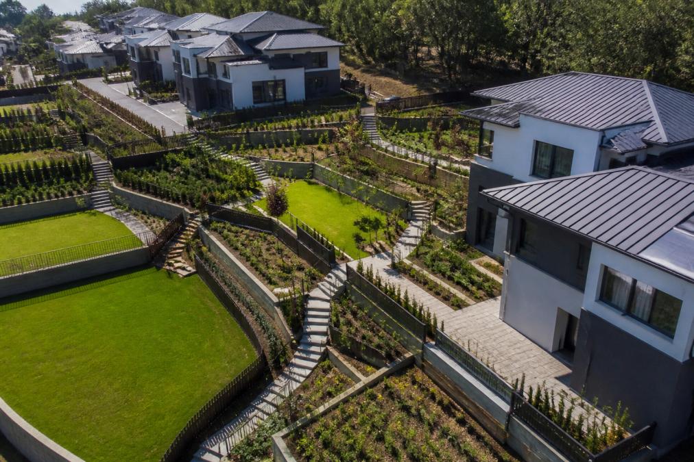 Aerial view of a residential development showing diverse hardscaping, paved pathways, garden beds and turf areas integrated across multiple properties with varied topography