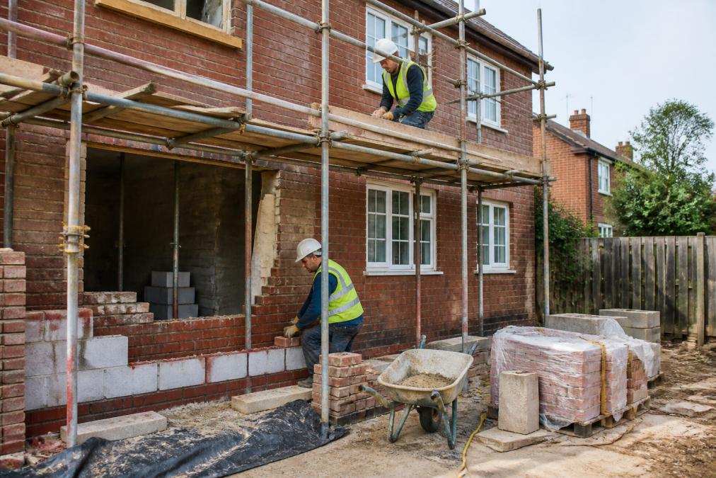 Professional construction team carrying out structural repairs on a residential brick property with scaffolding and materials visible, natural daylight illuminating the work site