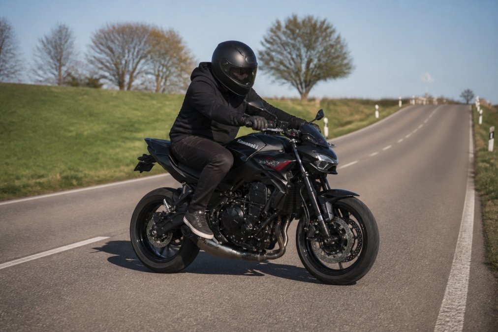 Ervaren motorrijder voert voorzichtige proefrit uit op tweedehands motor op lege landweg, test acceleratie en remmen in veilige omgeving met helder weer