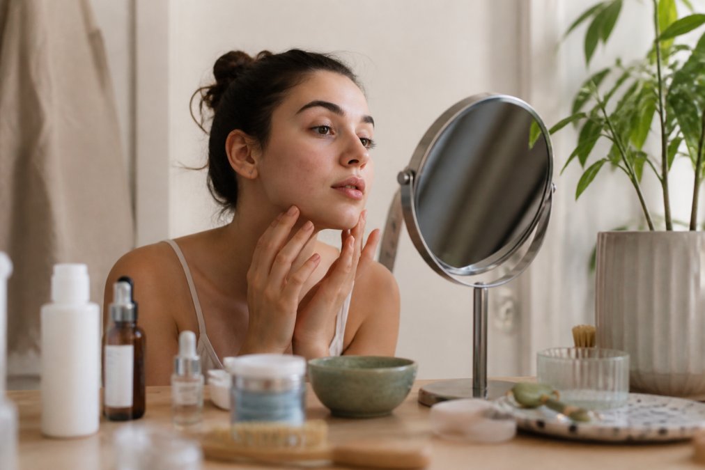 Young adult examining their skin in a mirror with natural light, assessing skin texture and considering their skincare approach