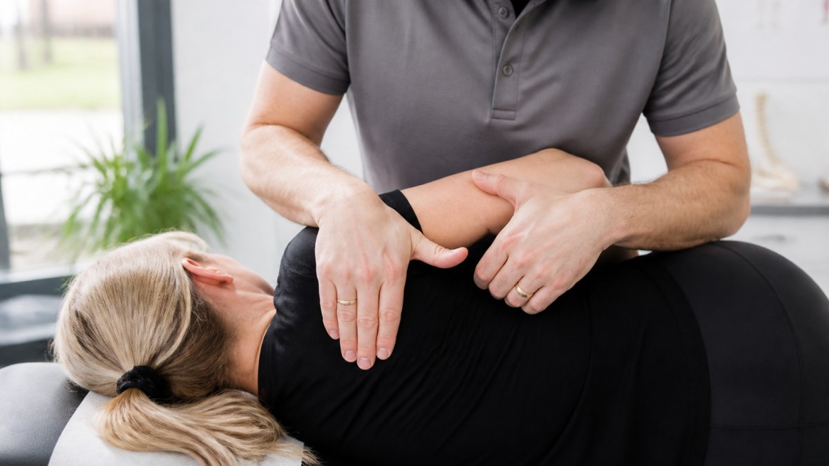 Professional chiropractor performing gentle spinal mobilisation technique on patient in calm clinical setting with soft lighting and relaxed patient posture