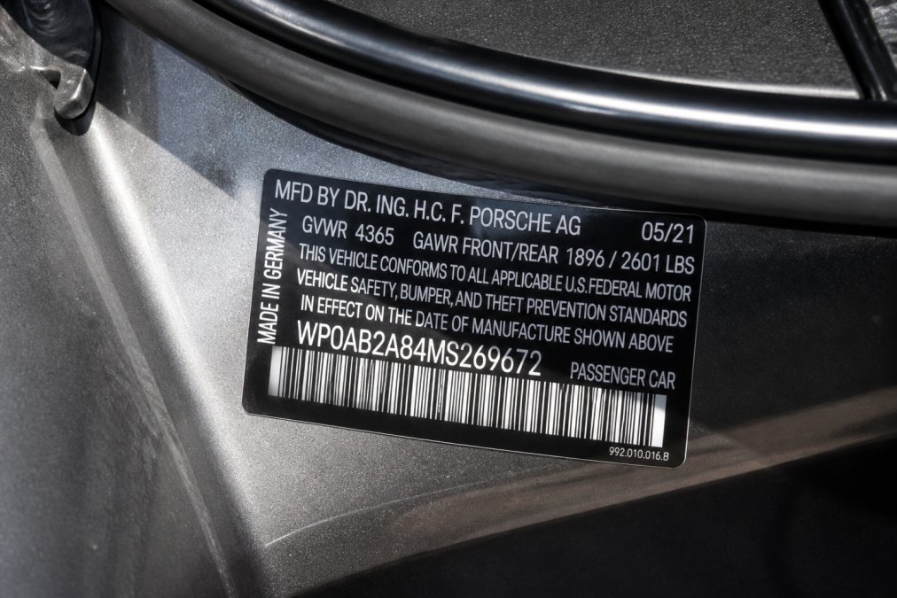 Close-up of a Porsche VIN plate on the driver's side door jamb, clearly showing the 17-character identification number with sunlight highlighting the characters