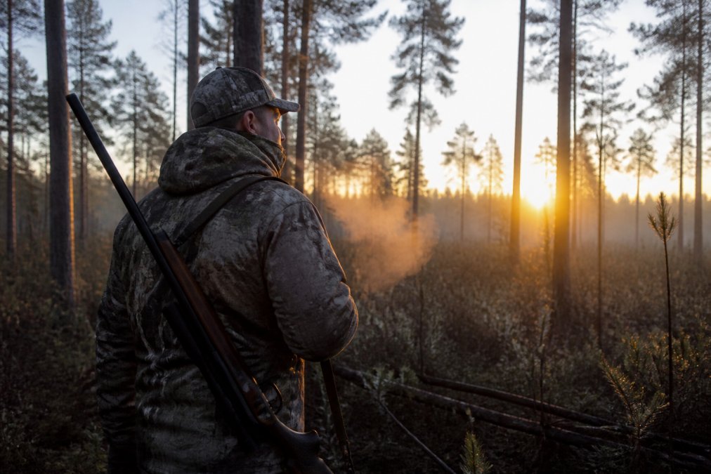 A hunter in full camo gear walking through a misty Georgia pine forest at sunrise, rifle slung over shoulder, breath visible in the cold air