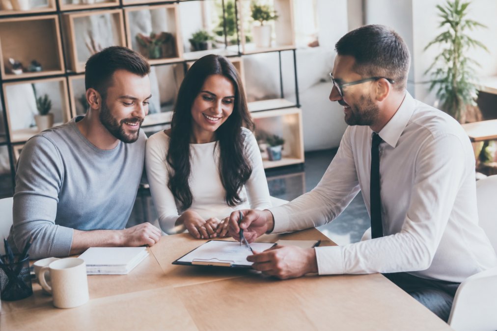 A friendly insurance agent sitting across from a couple at a desk, smiling and reviewing paperwork together in a well-lit office with warm natural lighting