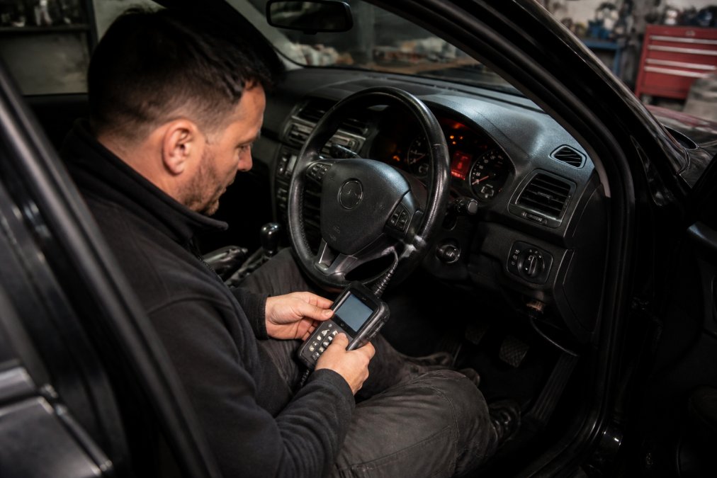Locksmith using a diagnostic tool to program spare car keys via the OBD-II port in a dimly lit garage