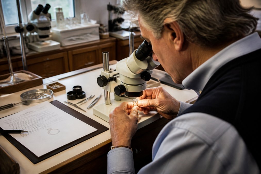 Gemologist examining a diamond ring under a microscope at a workbench with appraisal documents and professional tools