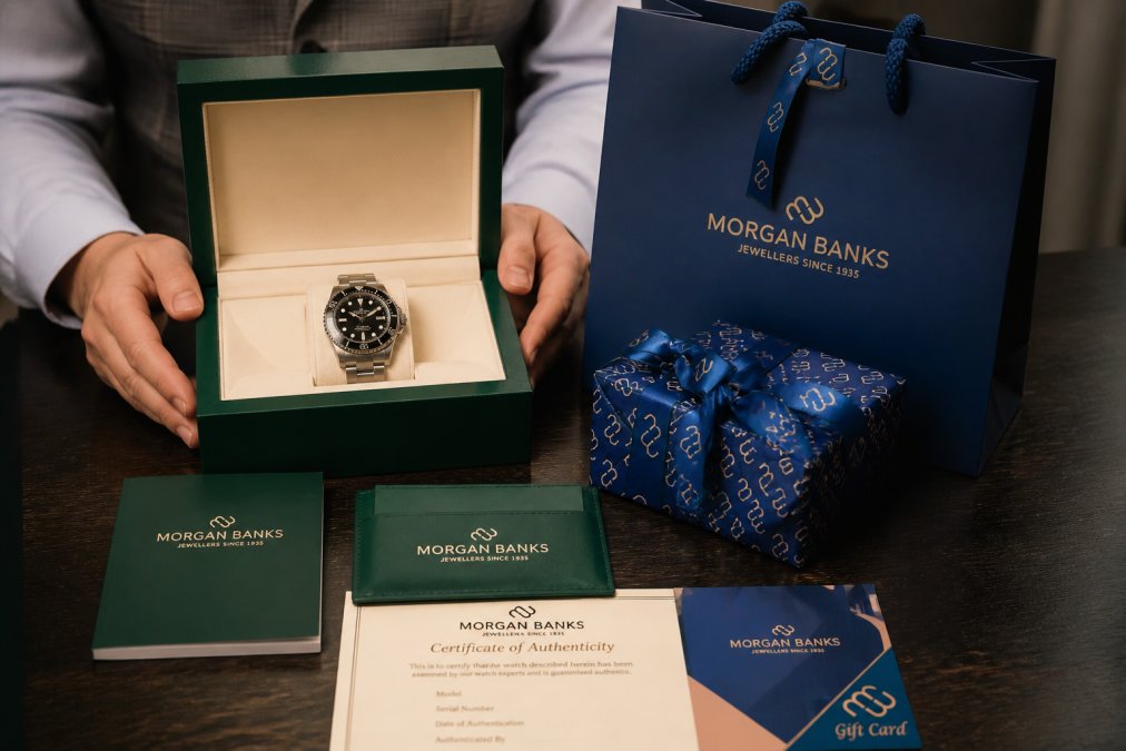 Close-up of hands carefully holding an authenticated luxury watch box with certification documents and warranty paperwork displayed on a dark wooden surface, showing professional presentation and care
