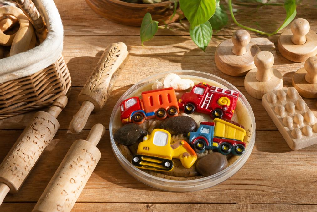 Een verzameling handgemaakte houten speelrollen en houten accessoires netjes gerangschikt op een warme houten tafel, met natuurlijk daglicht dat de houttextuur benadrukt, warme en rustgevende uitstraling