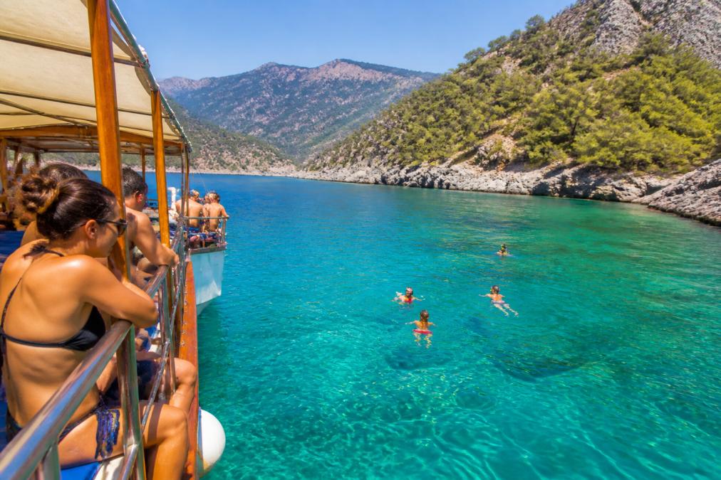 Fethiye tekne turunda turkuaz sularda yüzen insanlar ve gizli koy Fethiye manzarasına karşı teknede dinlenen gezginler.