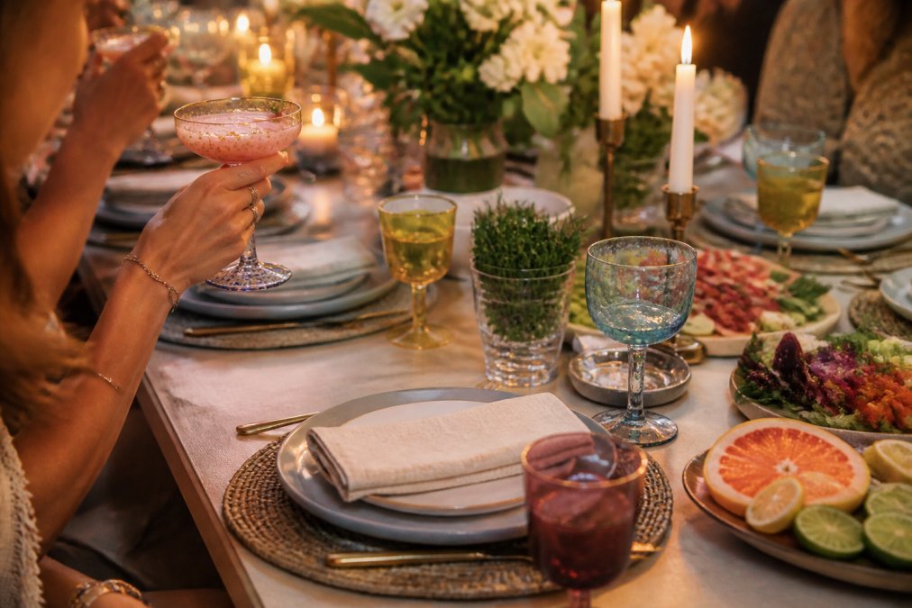 Elegant table setting with colorful handblown glassware filled with cocktails, surrounded by fresh garnishes and candles, showing how curated drinkware enhances a social gathering